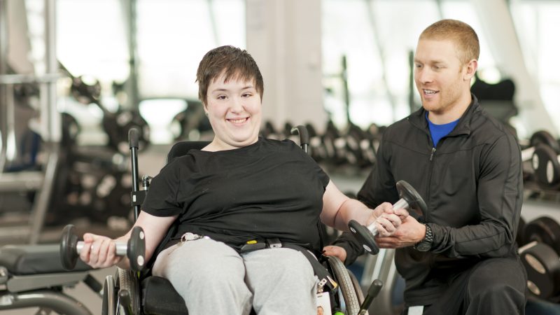 Disabled female in wheelchair exercising with trainer.