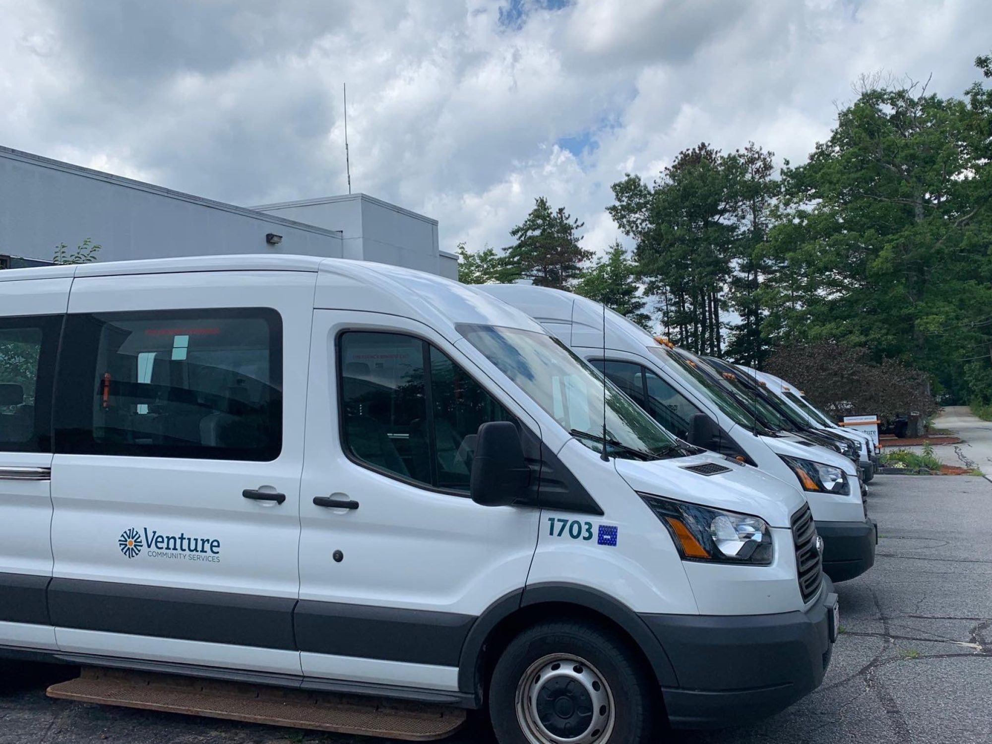 A row of white Venture Community Services transport vans parked outside a facility