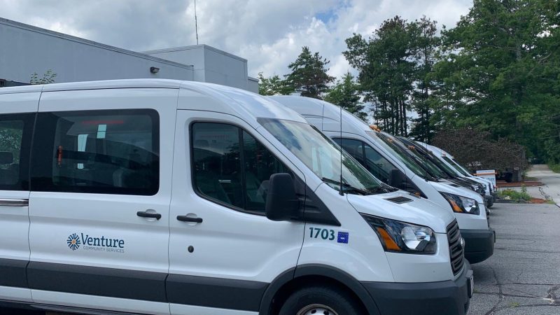 A row of white Venture Community Services transport vans parked outside a facility